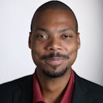 Portrait of a smiling African American man in a black suit against a white background.